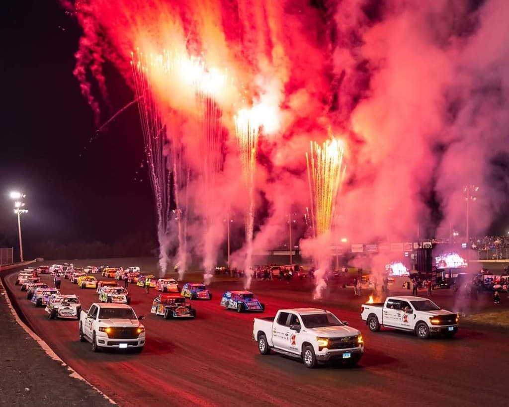Dirt track race cars lined up with fireworks